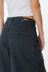 Jean de corte wide leg en color negro lavado, con tiro medio y cierre de botón y cremallera. Presenta bolsillos traseros amplios y etiqueta de cuero sintético con el logo de la marca en la parte posterior.