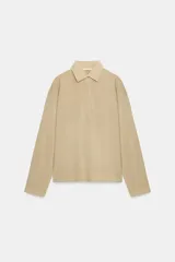 Polo oversize de algodón color beige, de manga larga, con cuello camisero y cierre frontal de botones ocultos.