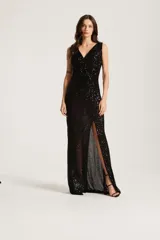 Vestido largo negro de fiesta con lentejuelas, escote en V cruzado, sin mangas y tajo pronunciado en la pierna izquierda.