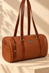 Cartera tipo baulito de cuero color marrón tostado, con doble asa larga de hombro, cierre superior y detalle de placa metálica con el logo de la marca en el centro.