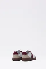 Zapatilla urbana de mujer con base de goma marrón, capellada en beige y blanco, y detalles bordados en color bordó. Cierre con cordones bordó.