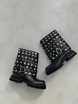 Bota corta de cuero negro con suela track, decorada con múltiples tachas metálicas circulares y rectangulares en toda la caña. Incluye una tira con hebilla metálica ajustable en la parte inferior.