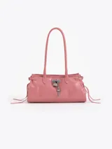 Cartera de hombro confeccionada en cuero vacuno con acabado brillante. Presenta un diseño rectangular con herraje metálico tipo candado y dijes decorativos en el frente, además de tiras laterales ajustables.