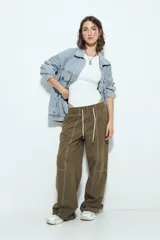 Pantalón tipo babucha de tiro bajo, color verde oliva, con silueta amplia y costuras visibles en contraste blanco. Posee cintura elástica con lazo blanco para ajuste.