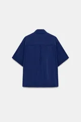 Camisa de cuello solapa y manga corta con dobladillo, presenta bolsillos de plastrón en el frente, bajo asimétrico y cierre frontal con botones ocultos.