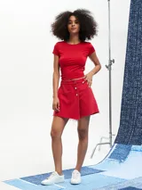 Short pollera de denim color rojo con diseño cruzado, cierre frontal de botones metálicos y acabado desmechado en el ruedo.
