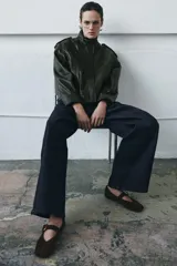 Bailarina plana confeccionada en ante color marrón, con diseño de punta cuadrada y cierre mediante una tira con hebilla metálica dorada en el empeine.