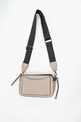 Bandolera de diseño rectangular en color beige con textura saffiano. Cuenta con una correa de hombro ajustable y extraíble de cinta negra, cierre superior y detalles metálicos en los enganches.