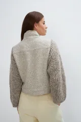 Campera de lana fina color crema, con cuerpo estructurado y mangas de tejido de punto acanalado. Presenta cuello alto, cierre frontal con botones y bolsillos laterales con doble abertura.