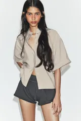 Camisa de corte fluido confeccionada en mezcla de modal, con cuello solapa, manga corta y bolsillo de plastrón en el delantero. Presenta cierre frontal con botones ocultos por tapeta y bajo con aberturas laterales.