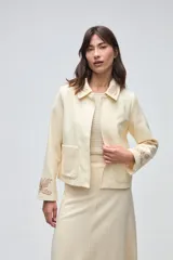Chaqueta de lana fina sin teñir, con cuello clásico y bolsillos frontales. Presenta detalles bordados en el cuello y en los puños de las mangas. Es una prenda forrada con diseño exclusivo.