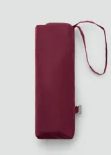 Paraguas plegable de tamaño mini, color bordó, con correa de mano integrada y cierre con broche metálico grabado.