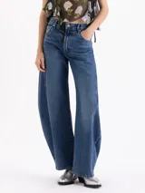 Jeans de tiro medio con silueta slouchy y corte amplio. Presenta recortes verticales que estructuran la prenda, generando volumen desde el muslo hasta la bota. Confeccionado en denim de lavado clásico con desgastes localizados.