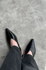 Zapato tipo flat destalonado de color negro con acabado brillante, punta fina y cierre con hebilla lateral.