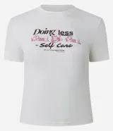 Remera de algodón con cuello redondo, mangas cortas y estampa en la espalda con diseño de un perro descansando en una reposera y la frase "Doing less is Self Care".