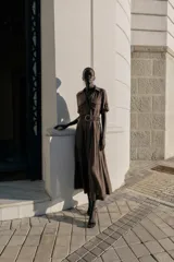 Vestido midi de corte fluido en color marrón, con cuello solapa, escote en pico y cierre frontal de botones. Presenta mangas cortas con dobladillo, bolsillos delanteros y un cinturón trenzado con hebilla redonda de madera.