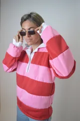 Sweater estilo rugby a rayas horizontales rosas y rojas con cuello blanco y cierre parcial con botones.