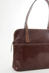 Cartera de hombro tipo portafolio confeccionada en cuero vacuno, con diseño estructurado que combina marrón liso y un panel frontal en cuero texturizado color mostaza. Posee doble asa larga y cierre superior.
