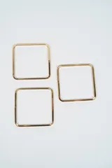 Set de tres brazaletes rígidos de forma cuadrada con acabado metálico dorado.