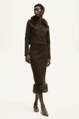 Saco corto de punto fino color marrón oscuro, con cuello de pelo sintético marrón oscuro y cierre frontal de botones metálicos. Posee bolsillos delanteros insertados.