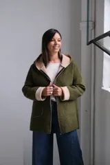 Tapado de paño color verde oliva con interior y detalles en beige. Presenta capucha amplia, cierre frontal, bolsillos laterales y mangas con puños vueltos que dejan ver el contraste de color.
