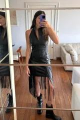 Minifalda negra de cuero ovino con flecos largos, cierre trasero y ojalillos dorados.