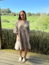 Vestido corto de lino color beige claro, con cuello mao, escote con botones de nácar, mangas tres cuartos con volados y ruedo con volado.