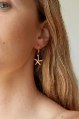 Aros tipo argolla pequeña con dije colgante en forma de estrella de mar, elaborados en acero quirúrgico.