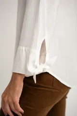 Camisa blanca de manga larga con cuello mao y cierre frontal con botones. Las mangas tienen nudos decorativos en los puños.