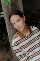 Remera de manga larga con cuello polo y cierre frontal de botones. Presenta un diseño a rayas horizontales en tonos bordó, blanco y celeste.