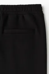 Jogging sastrero color negro de corte regular, confeccionado en mezcla de algodón de peso medio. Cuenta con cintura elástica con cordón ajustable, bolsillos laterales y pliegues delanteros cosidos.