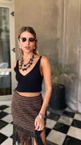 Falda tejida a mano en crochet, con diseño a rayas horizontales en tonos marrón y negro con hilos de lurex dorado. El ruedo presenta una cascada de flecos largos y finos en color negro.