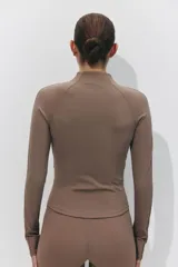 Campera deportiva de corte ajustado, color marrón tostado, con cuello elevado, cierre frontal completo, mangas raglán con abertura para el pulgar y bolsillos laterales con cierre.