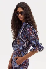 Camisa estampada con flores y motivos geométricos en tonos azules, marrones y naranjas. Tiene cuello mao, mangas 3/4 con volados y detalles de encaje en los hombros y mangas.