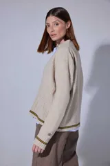 Saco tejido en lambswool con diseño de rombos y trenzas en el frente. Presenta cierre frontal con botones, cuello en V y detalles de rayas en contratono en puños y ruedo. Incluye pin bordado en la manga.