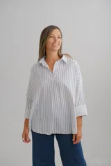 Blusa de corte holgado con estampado de rayas verticales azules sobre fondo blanco. Presenta cuello camisero con escote en V y mangas largas amplias con puños vueltos.