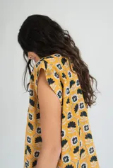 Vestido corto sin mangas en color rosado con estampado floral en blanco y negro. Presenta una cartera de botones asimétrica en el frente y detalle de volado fruncido en el ruedo. Confeccionado en algodón liviano.