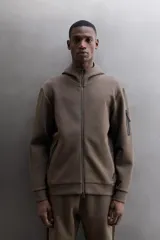 Campera canguro de Zara Athleticz, modelo relaxed fit, confeccionada en tejido técnico compacto elástico con mezcla de algodón en color azul marino. Cuenta con cuello subido con capucha, manga larga con bolsillo lateral con cierre, bolsillos frontales con cierre y acabado termofijado, cierre frontal de doble dirección y logo estampado en el bajo.