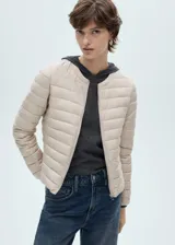 Campera acolchada de cuello redondo y manga larga con puños elásticos. Presenta cierre frontal de cremallera y dos bolsillos laterales con cierre.