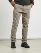 Pantalón de vestir verde oliva, de corte slim fit, sin pinzas, con bolsillos laterales y traseros. Se ajusta a la cintura con cinturón de cuero marrón.