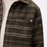 Camisa de manga larga Rusty modelo Taton, confeccionada en tejido de franela con diseño de rayas horizontales en tonos verdes y marrones. Presenta cuello clásico, cierre frontal con botones y bolsillos en el pecho.