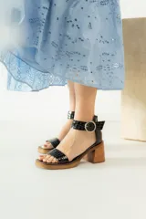 Sandalias de cuero negro con textura de reptil, diseño de dos tiras, una en el empeine y otra con hebilla ajustable en el tobillo. Poseen una plataforma y taco cuadrado de madera.