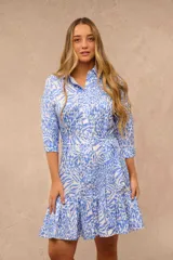 Vestido corto camisero con estampado animal print en tonos celeste y blanco, de manga tres cuartos, con cierre frontal de botones, lazo ajustable en la cintura y detalle de volados en el ruedo.