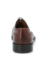 Zapato de vestir tipo Oxford con diseño brogue, confeccionado en cuero vacuno de color marrón. Presenta cierre mediante cordones, puntera redondeada con detalle de perforaciones decorativas y suela mixta de cuero y goma.