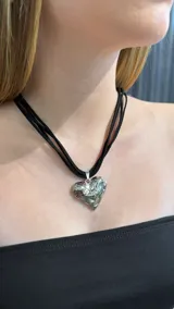 Gargantilla tipo choker con tiras negras de gamuza y dije central en forma de corazón con acabado metálico plateado y textura irregular.