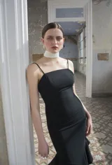 Vestido midi negro de corte sirena al cuerpo, con escote recto, tirantes finos y falda con volados en el bajo.