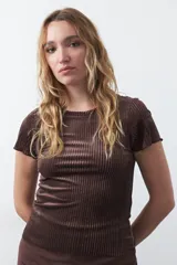 Top de manga corta confeccionado en terciopelo negro, con textura acanalada y acabado con leve brillo. Presenta un diseño ajustado al cuerpo con cuello redondo.