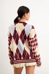 Saco liviano oversize de punto con diseño de rombos argyle y flores celestes sobre fondo marrón, rojo y crema, con cierre frontal de botones y cuello redondo.