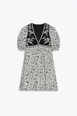 Vestido corto con estampado floral en blanco y negro, escote pico, mangas cortas abullonadas y detalle de chaleco negro con bordados y falsos botones delanteros. Incluye forro interior.