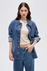 Sobrecamisa de jean azul medio, de corte oversize, con mangas largas y detalles de tachas decorativas en la parte frontal y trasera.
